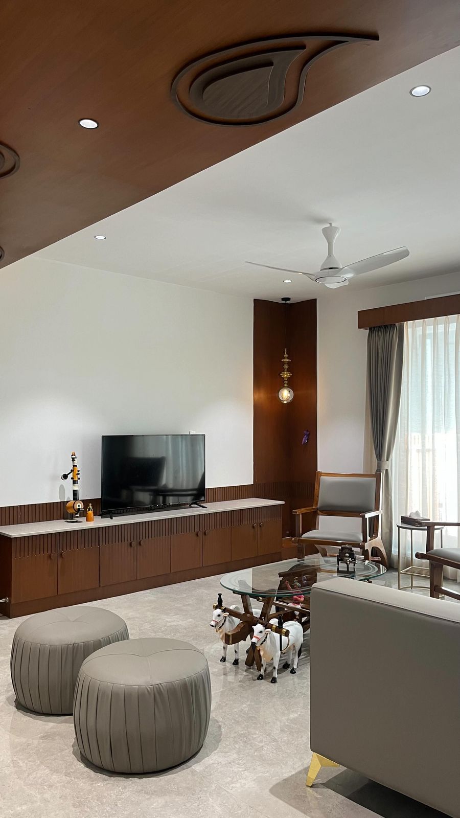 Living room with a carved teak ceiling detail, timber TV console and grey pouffes