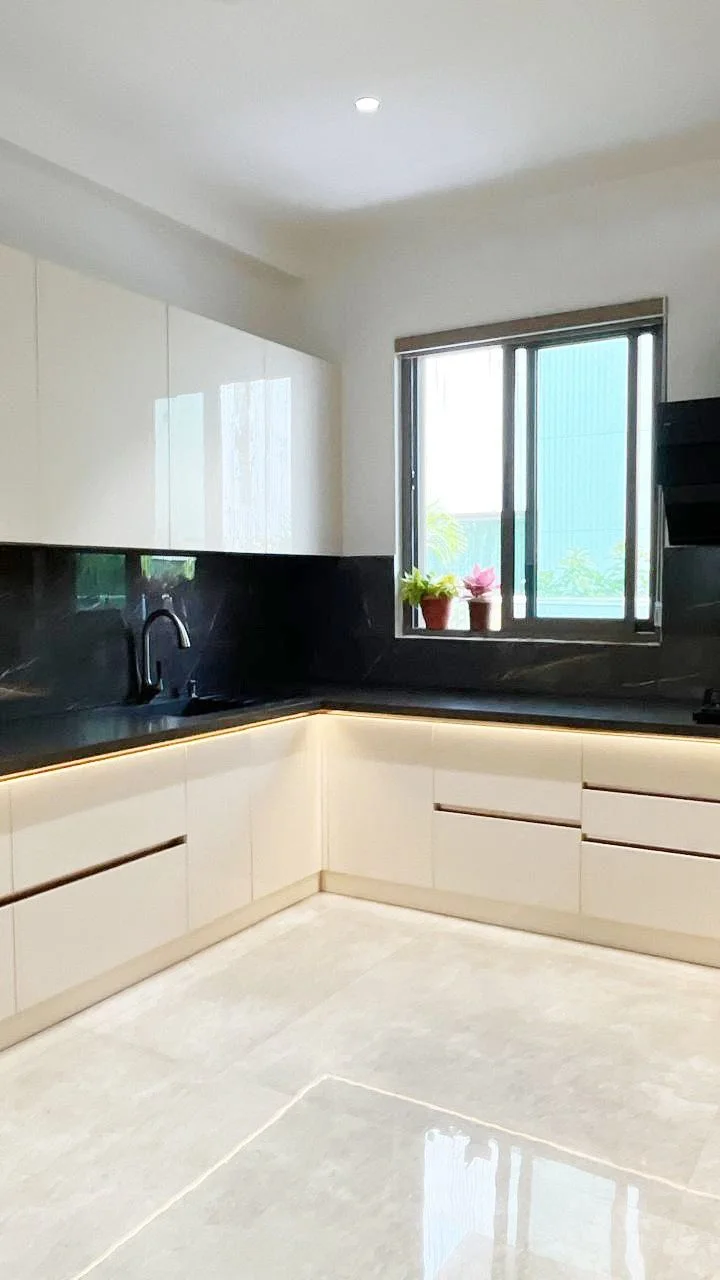 An'teak Villa, Hyderabad — L-shaped modular kitchen with white high-gloss shutters and a black marble countertop and backsplash